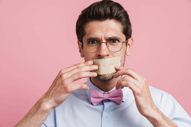 Young white man wearing bow tie posing with moth glued shut isolated over pink background - Фото, зображення