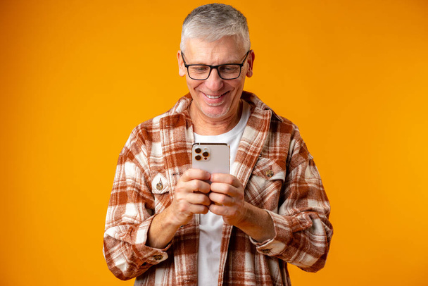 Senior smiling man using smartphone over yellow background - Zdjęcie, obraz