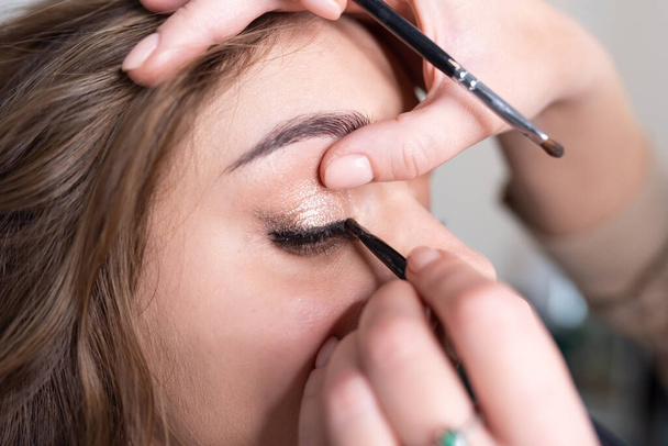 Make-up artist applies eyeliner to the girl's upper eyelid with a brush. High quality photo - Foto, Imagem