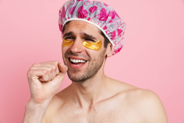 Young shirtless man wearing shower cap singing and gesturing isolated over pink background - Zdjęcie, obraz