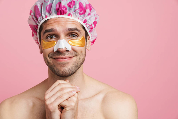 Young shirtless man with eye and nose patches smiling at camera isolated over pink background - Fotoğraf, Görsel