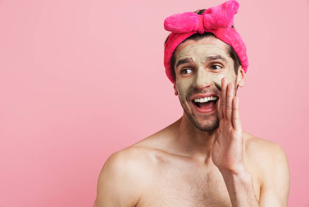 Young shirtless man wearing headband smiling and screaming at camera isolated over pink background - Foto, imagen