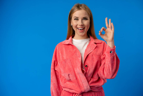 Young caucasian woman isolated on blue background showing ok sign - Fotoğraf, Görsel