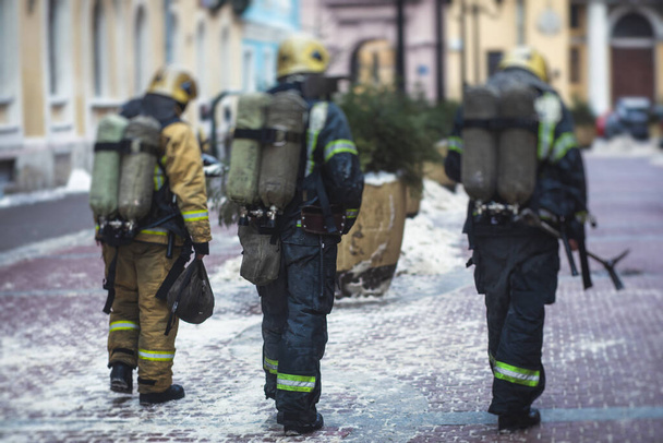 Group of fire men in uniform during fire fighting operation in the city streets, firefighters with the fire engine truck fighting vehicle in the background, emergency  - Valokuva, kuva