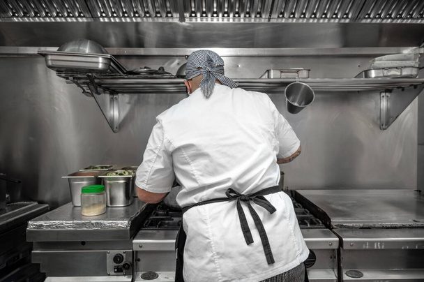 Back view of woman chef cooking food in the kitchen of a restaurant. - 写真・画像