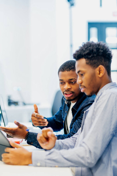 Két fekete férfi cseveg és egy projektről tárgyal a munkahelyén. fiatal fekete srácok használják technológia főiskolai campus - Fotó, kép