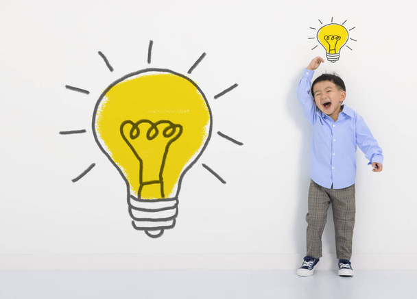 白い壁に子供の学生の思考や電球。かわいい男の子は新しいアイデアを持っています。イノベーション技術と教育の概念 - 写真・画像