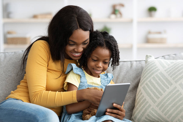 Τεχνολογίες για αναψυχή. Ευτυχισμένη μαύρη μητέρα και η μικρή κόρη χρησιμοποιώντας ψηφιακή ταμπλέτα - Φωτογραφία, εικόνα