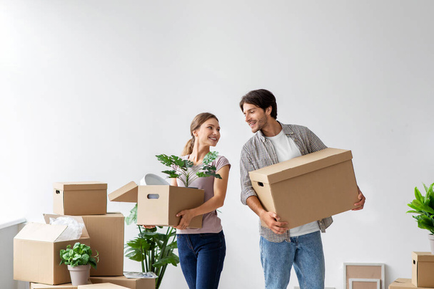 Glad happy young caucasian guy and lady in casual enjoy moving at new renting home in room with cardboard boxes - Photo, Image