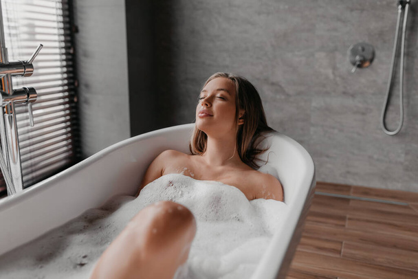 Tranquillo signora godendo bagno caldo con bolle di sapone, rilassante nella vasca da bagno con gli occhi chiusi dopo dura giornata, spazio libero - Foto, immagini