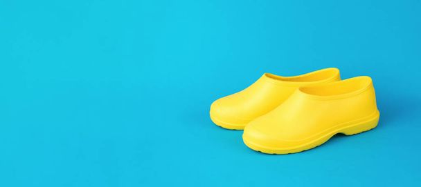 Mavi arka planda parlak sarı kauçuk galoşların minimum bileşimi. Islak hava için ayakkabılar. Metin için boşluk. - Fotoğraf, Görsel