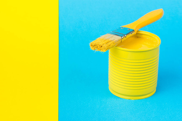 A jar with bright yellow paint and a brush on a blue background and a yellow strip of paper. Trending colors. Minimal concept of interior selection. - 写真・画像
