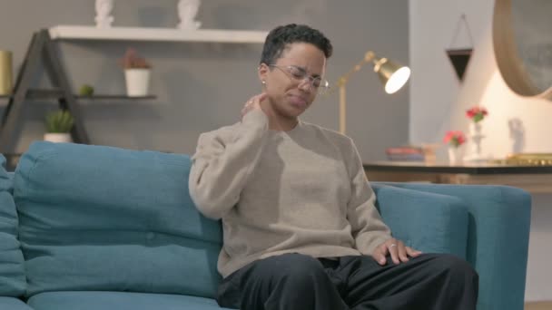Mujer africana teniendo dolor de cuello mientras está sentada en un sofá  - Metraje, vídeo