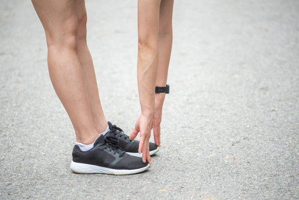 Rajatut kuvakaappaus näkymä juoksija nainen tekee venyttely ja lämpeneminen jalkansa ennen juoksemista. Venyttely voi lisätä joustavuutta ja vähentää loukkaantumisriskiä.  - Valokuva, kuva