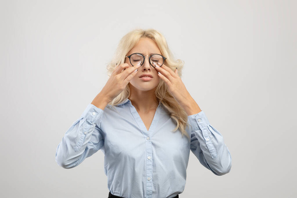 Müde Büroangestellte, die Augen berührt, Brille trägt und unter Augenüberlastung leidet, Sehprobleme hat - Foto, Bild