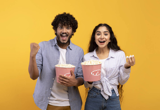 Excited indian man and woman eating popcorn, watching movie or football game, celebrating success of their team - Photo, Image