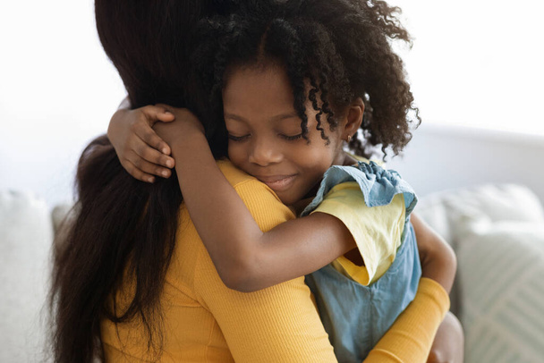 Χαριτωμένο κοριτσάκι Αφρο-Αμερικανίδα που αγκαλιάζει τη μαμά της στο σπίτι - Φωτογραφία, εικόνα