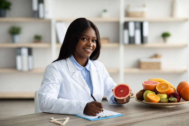 Vidám dietetikus nő étkezési tervet készít az ügyfélnek, a fogyókúrás klinikán dolgozik, mosolyog a kamerára - Fotó, kép
