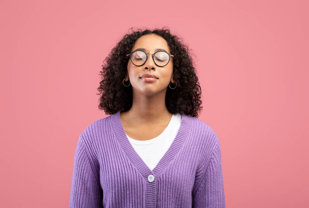 Nyugodt fiatal fekete nő szemüvegben csukja be a szemét, lélegzik szabadon rózsaszín stúdió háttér - Fotó, kép