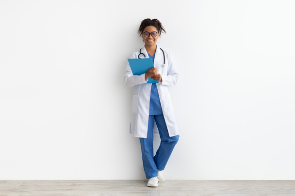 Portrait of black doctor posing with clipboard at white studio - Photo, Image