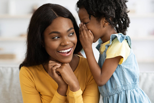Söpö pieni musta tyttö kuiskaa jotain hänen onnellinen Mommys korva - Valokuva, kuva