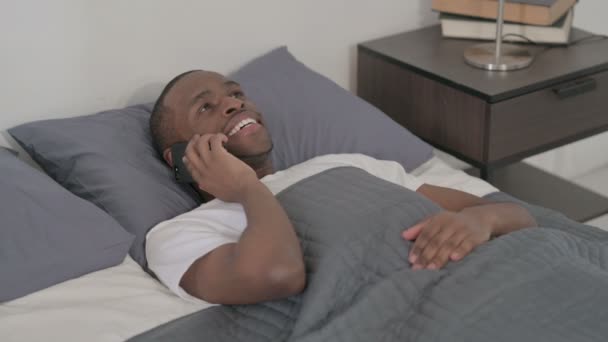 African Man Μιλώντας στο Smartphone, ενώ κοιμάται στο κρεβάτι, κοντινό - Πλάνα, βίντεο