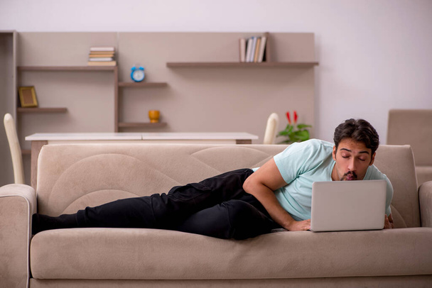 Молодой человек сидит на диване с компьютером дома - Фото, изображение