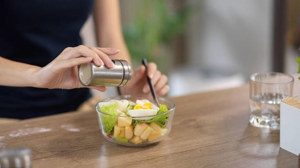 Großaufnahme, eine Frau, die Salz in ihre gesunde Salatschüssel am heimischen Esstisch gibt. Gesundes und diätetisches Ernährungskonzept - Foto, Bild