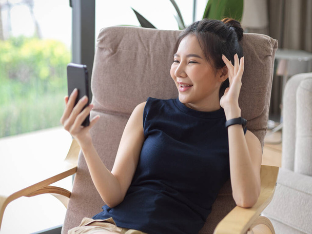 Glücklich asiatische junge Frau verbringen ihren freien Tag zu Hause, genießen Videotelefonie mit ihren Freunden im Wohnzimmer. - Foto, Bild