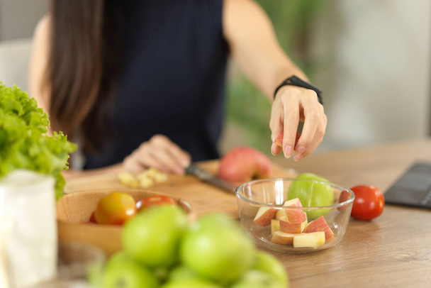 Közelkép, egy nő, aki egészséges ételeket készít, almát szeletel, salátástálat készít a konyhában.. - Fotó, kép