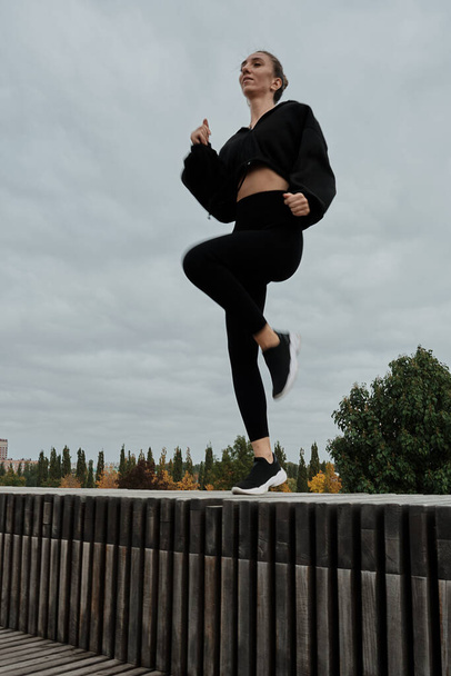 Nainen mustassa verryttelypuvussa urheilee puistossa. - Valokuva, kuva