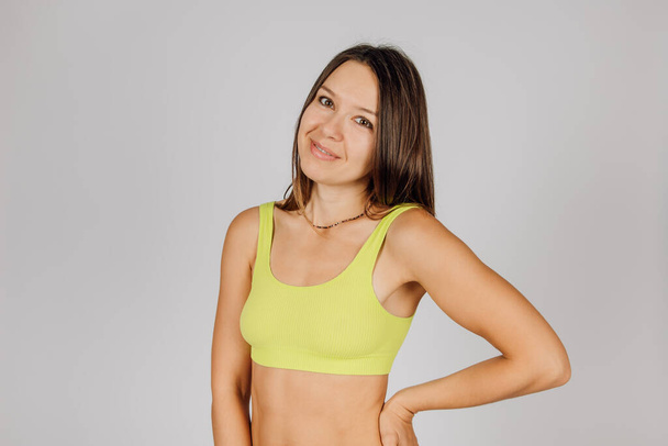 Portrait of beautiful Caucasian woman. Beautiful elegant tanned brunette in yellow underwear, smiling at camera, posing on isolated gray background, concept of body acceptance and beauty - Photo, image