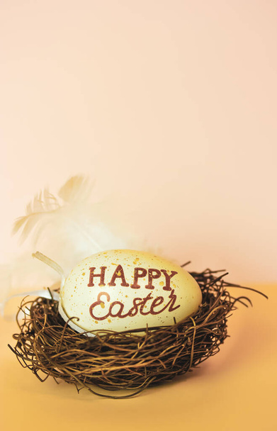 Egg in bird's nest with text Happy Easter on light brown background with space for text. Spring religious holidays. Easter celebration backdrop with space for your text. April holiday. Vertical photo. - Photo, image