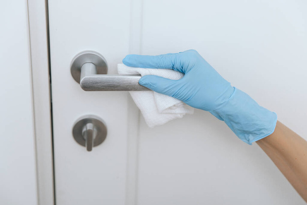 Cleaning black door handles with an antiseptic white wet wipe and sanitizer spray. Sanitize surfaces prevention in hospital and public spaces against corona virus. Woman hand using towel for cleaning - Photo, Image