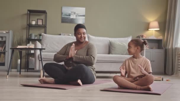 Afrika kökenli Amerikalı genç bir kadın ve 5 yaşındaki güzel kızı evde yoga minderinde birlikte meditasyon yapıyorlar. - Video, Çekim