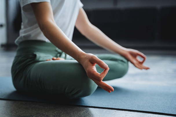 A young girl sits in the lotus position of her hand on her lap, her fingers folded into the rank of mudra. Time of Zen, immersion inward, solitude, alone at home, tranquility and peace - Fotó, kép