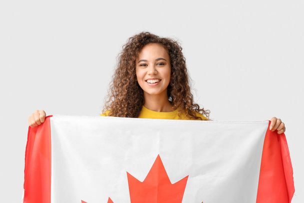 Beautiful young African-American woman with Canadian flag on light background - Fotoğraf, Görsel