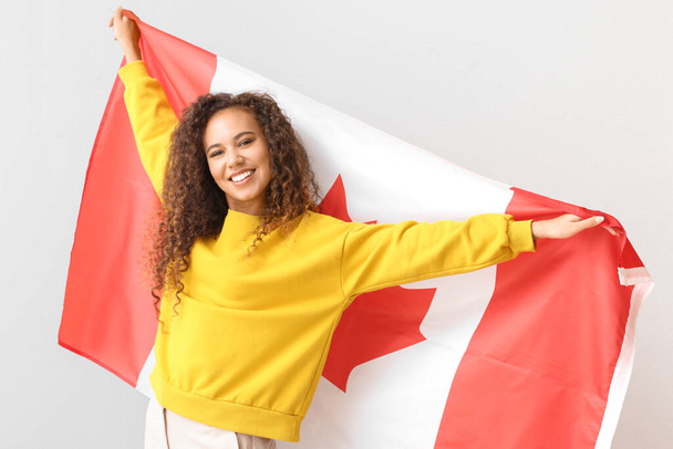 Piękna młoda Afroamerykanka z kanadyjską flagą na jasnym tle - Zdjęcie, obraz