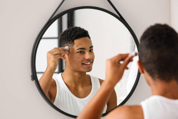 若いアフリカ系アメリカ人の男はバスルームでスキンケアのための血清を使用して - 写真・画像