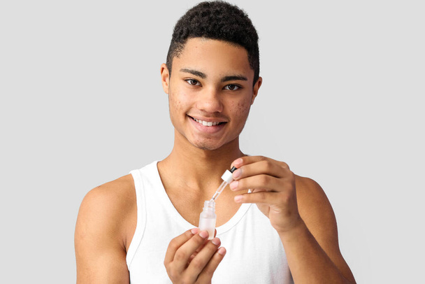 Junger Afroamerikaner mit Serum zur Hautpflege auf grauem Hintergrund - Foto, Bild