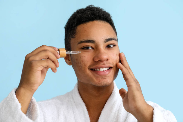 Молодий афроамериканець з сироваткою для догляду за шкірою на кольоровому фоні - Фото, зображення
