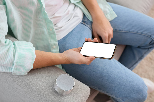 Man connecting mobile phone to wireless portable speaker on sofa, closeup - Photo, Image