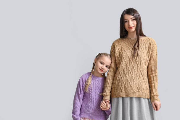 Little girl and her mother in warm sweaters holding hands on light background - Fotoğraf, Görsel