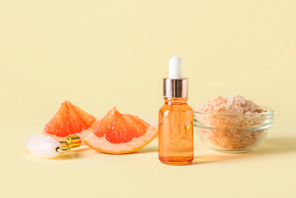 Botella de aceite esencial de pomelo, sal marina y herramienta de masaje facial sobre fondo de color - Foto, Imagen