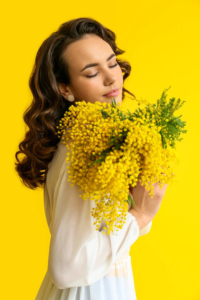 Beautiful young woman with mimosa flowers on yellow background - Fotoğraf, Görsel