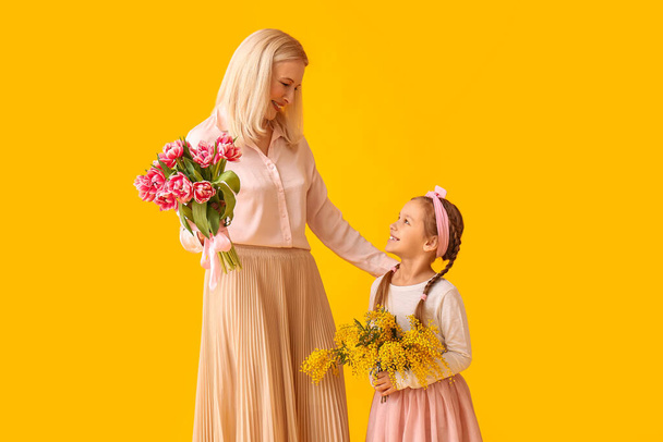 Маленька дівчинка з бабусею і квітами на жовтому тлі. Міжнародний жіночий день - Фото, зображення