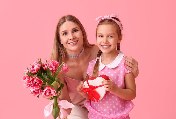Little girl, her mother with tulips and gift on pink background - Foto, afbeelding