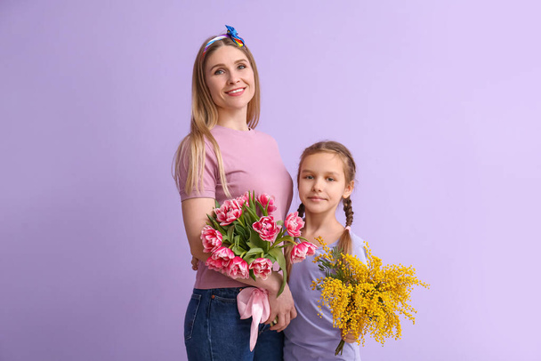 Little girl with her mother and flowers on lilac background - Photo, Image