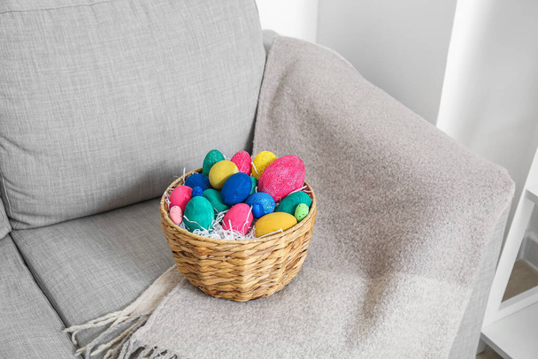 Wicker basket with Easter eggs on sofa near light wall - Photo, image