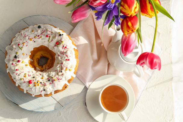 Gâteau de Pâques savoureux, tasse de thé et vase avec des fleurs sur fond clair - Photo, image
